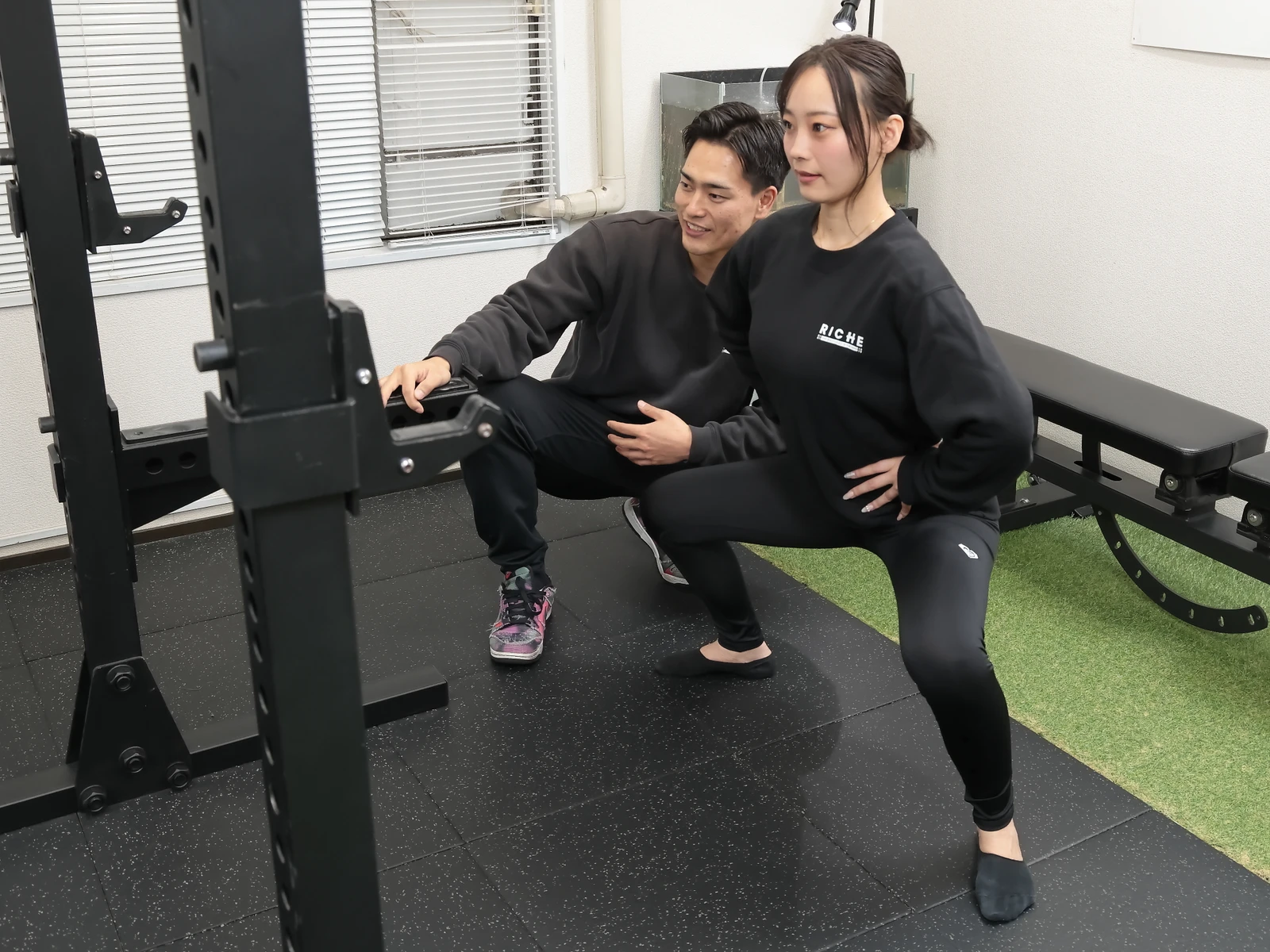 RICHEのジムで女性が男性トレーナーとスクワットのフォームを確認する様子